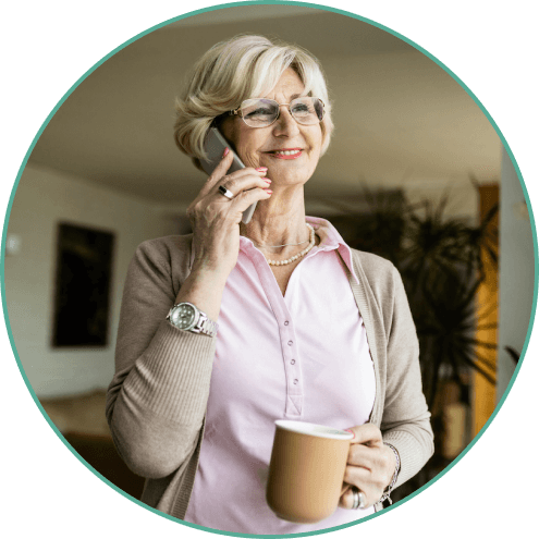 elderly woman smiling while on the phone and holding a cup of coffee