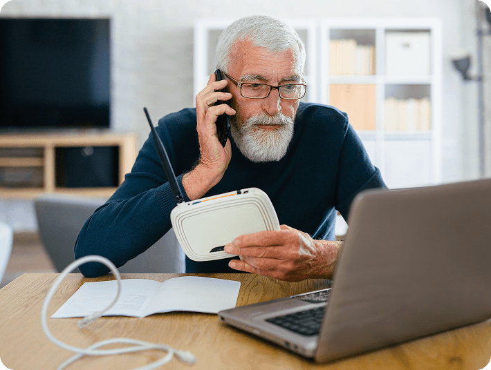 older man on the phone while troubleshooting a wireless router at his laptop